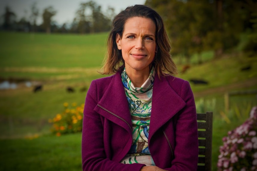 Woman in purple jacket in front of paddock full of cows.