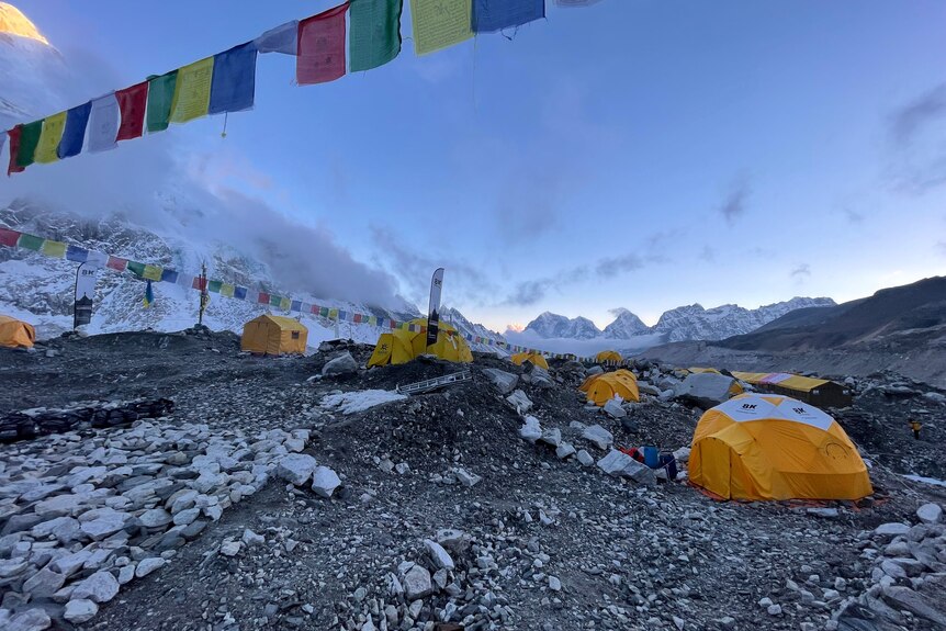 Orange expedition tents pitched on glacial morraine, with prayer flags flying in the foreground. 