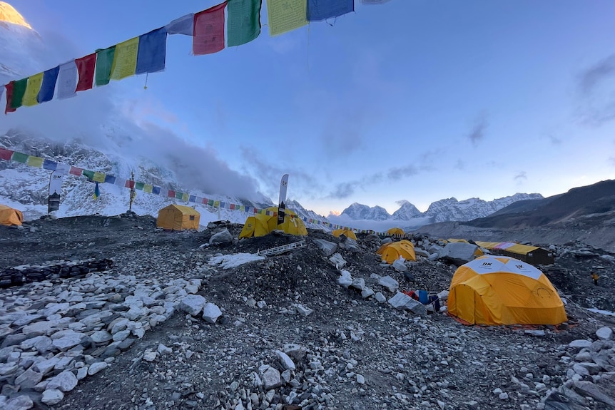 Orange expedition tents pitched on glacial morraine, with prayer flags flying in the foreground. 