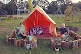 two kids sit in a camp set up in their back yard with an orange tent