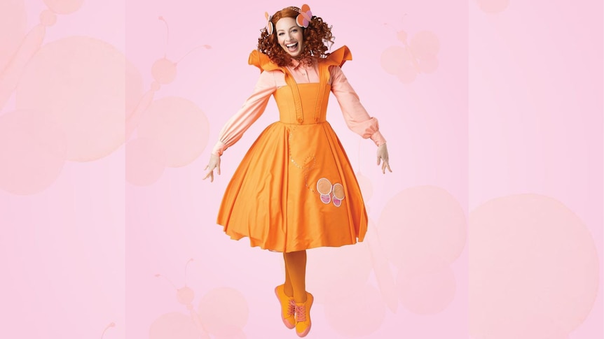 Emma Watkins jumps in an orange dress and shoes on a pink background.