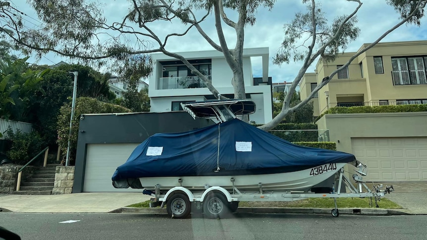 A boat on a trailer parked in front of a mansion.