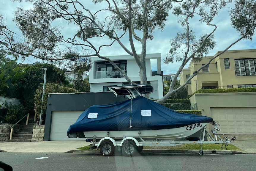 A boat on a trailer parked in front of a mansion.