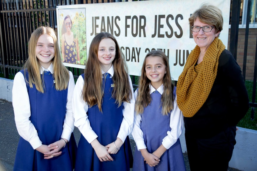 Three girls in school uniform and a woman standing in front of a banner with a picture of a girl in a sunflower dress