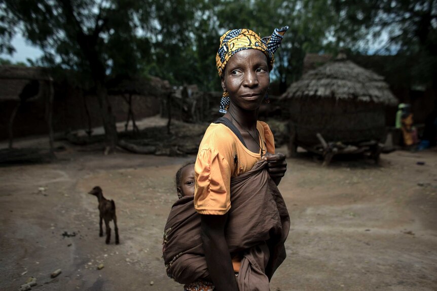 A woman in Nigeria is pictured carrying her baby on her back in the middle of a poverty stricken town.