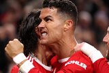 Cristiano Ronaldo grimaces and clenches his fist while being hugged by two teammates