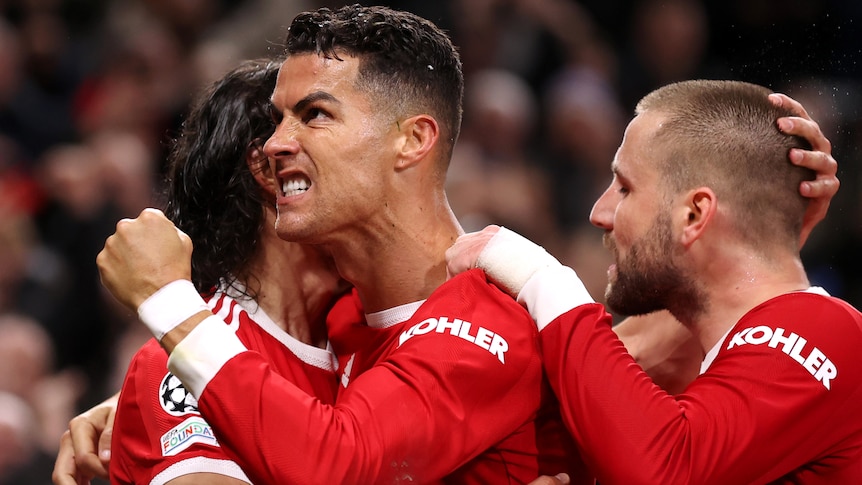 Cristiano Ronaldo grimaces and clenches his fist while being hugged by two teammates