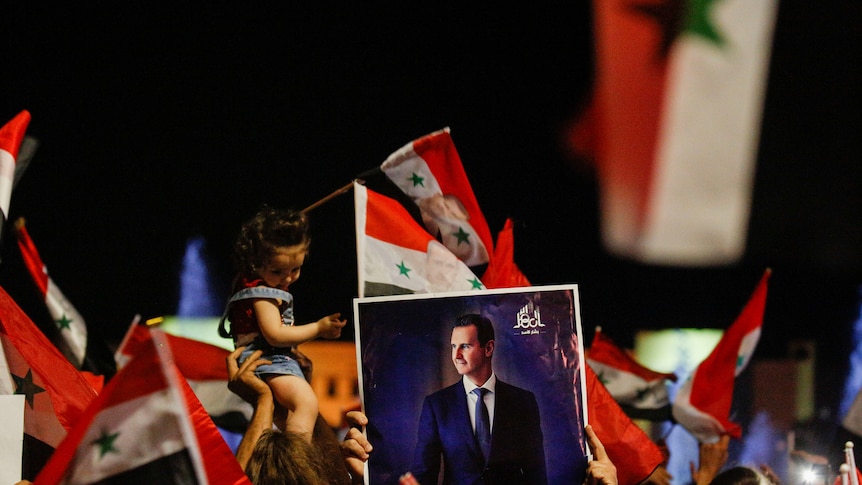 A small child and a picture of Bashar al-Assad held above a crowd of people celebrating.
