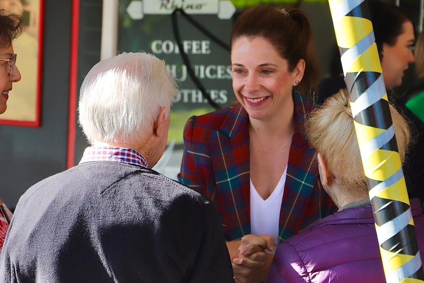 a woman parliamentarian out on the streets shaking the hand of an elderly m,an and woman