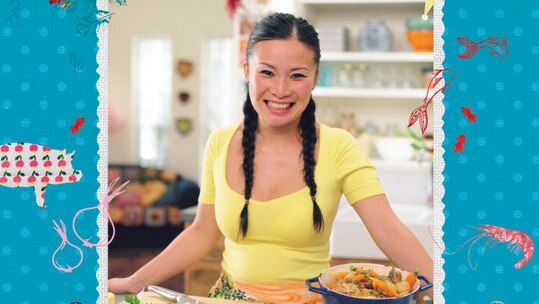 Poh Ling Yeow smiles at the camera while standing behind a bench top full of vegetables.