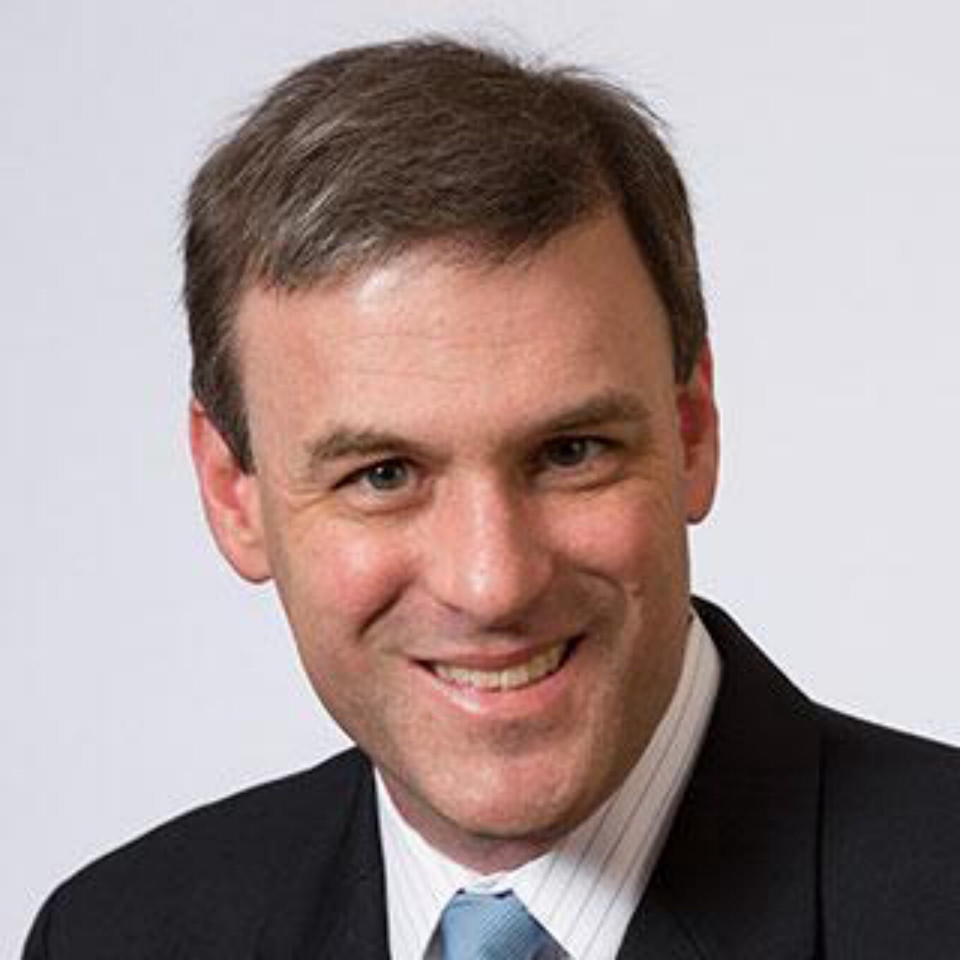 A portrait of Doug Levin. He is smiling at the camera and wearing a dark business suit, white shirt anda blue tie. 
