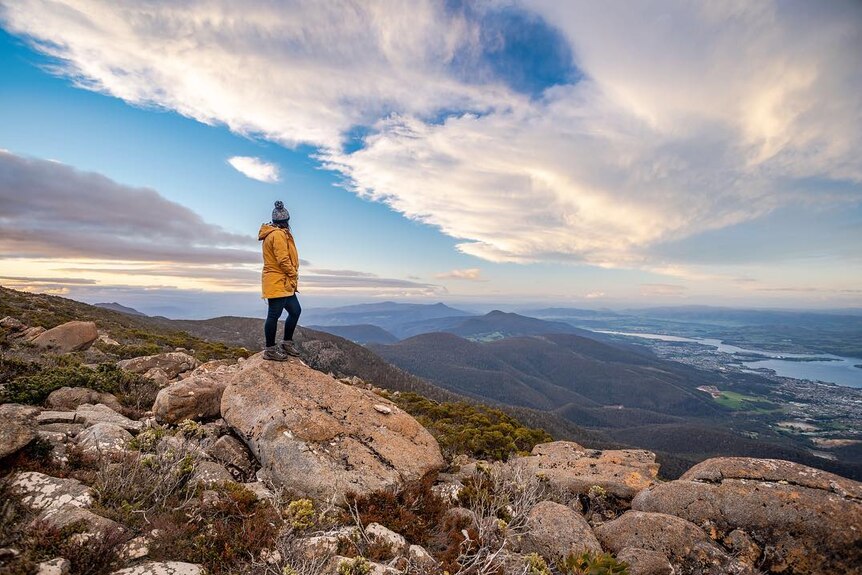 A person stands on the top of kunanyi/Mount Wellington wearing warm clothes.