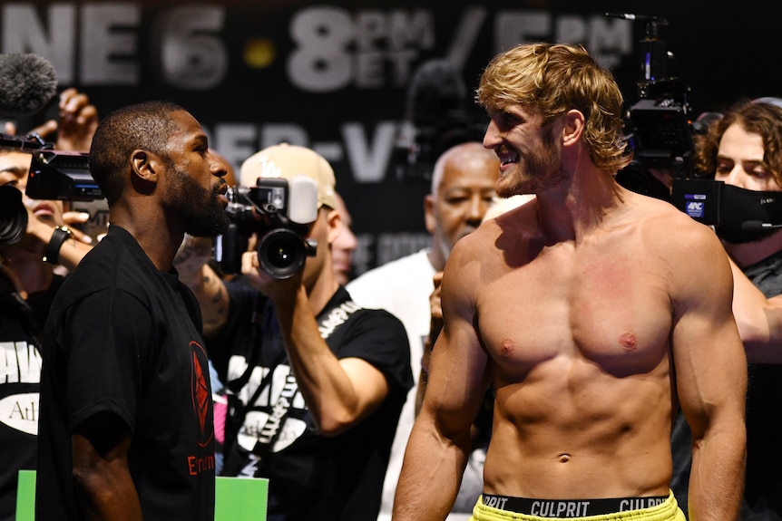 Two boxers stare at each other as photographers aim their cameras at them in the background.