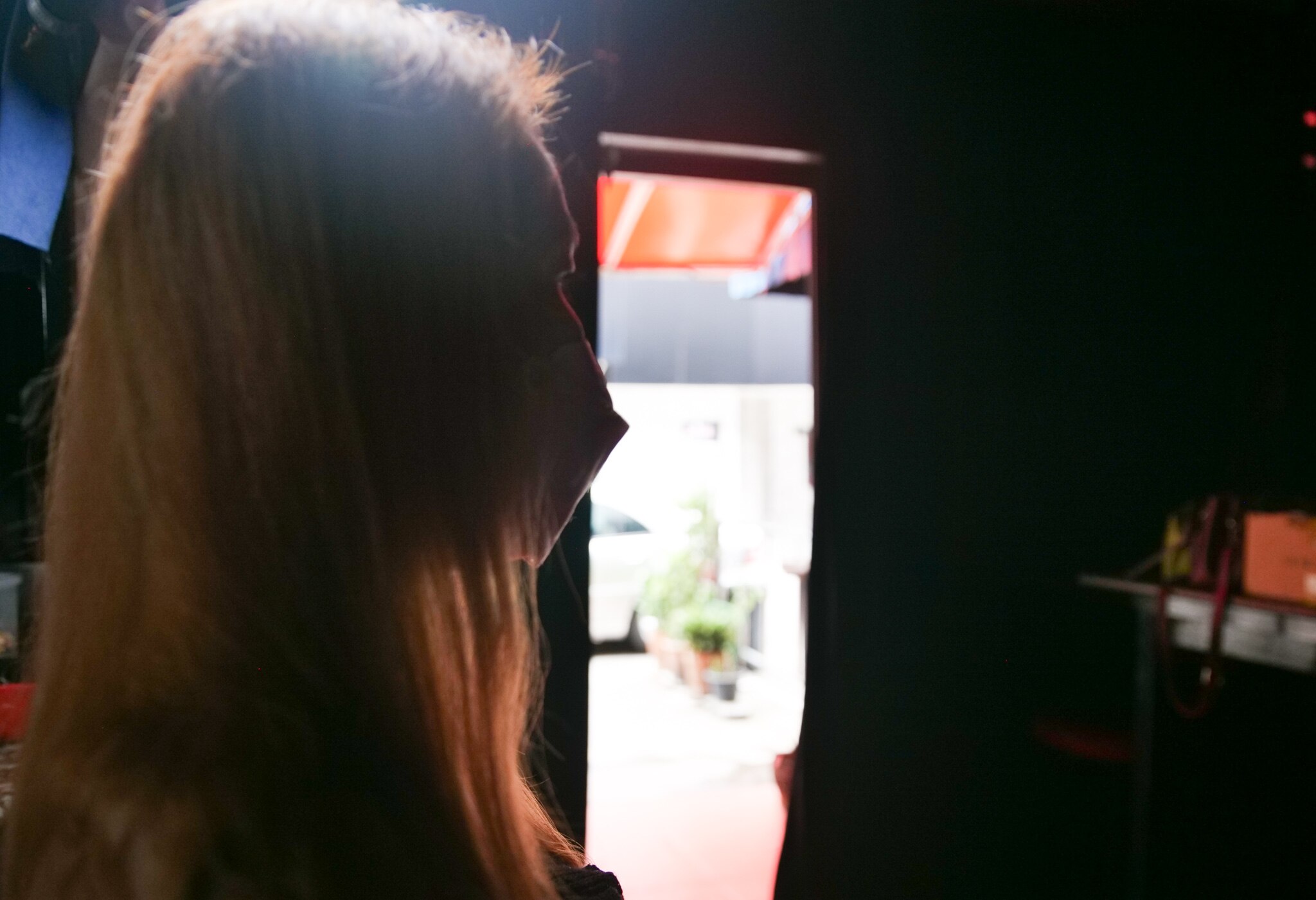 A woman with blonde hair and wearing a mask looks outside.