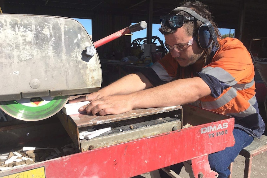 A mining support worker wearing ear and eye protection cuts tiles with a machine.