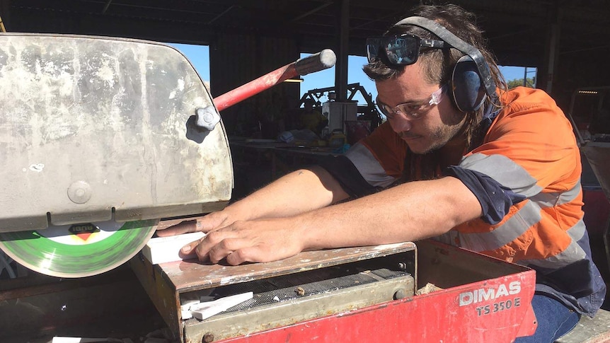 A mining support worker wearing ear and eye protection cuts tiles with a machine.