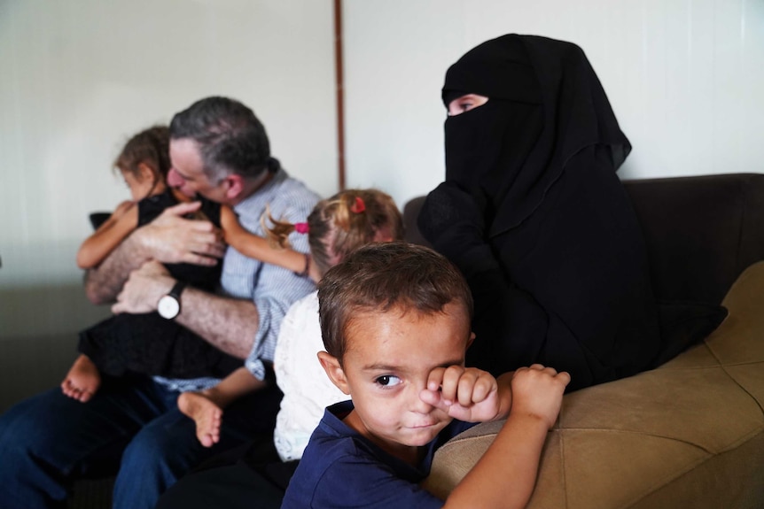 Kamalle Dabboussy's grandson sits wiping his eye with Kamalle in the background cuddling his sister.