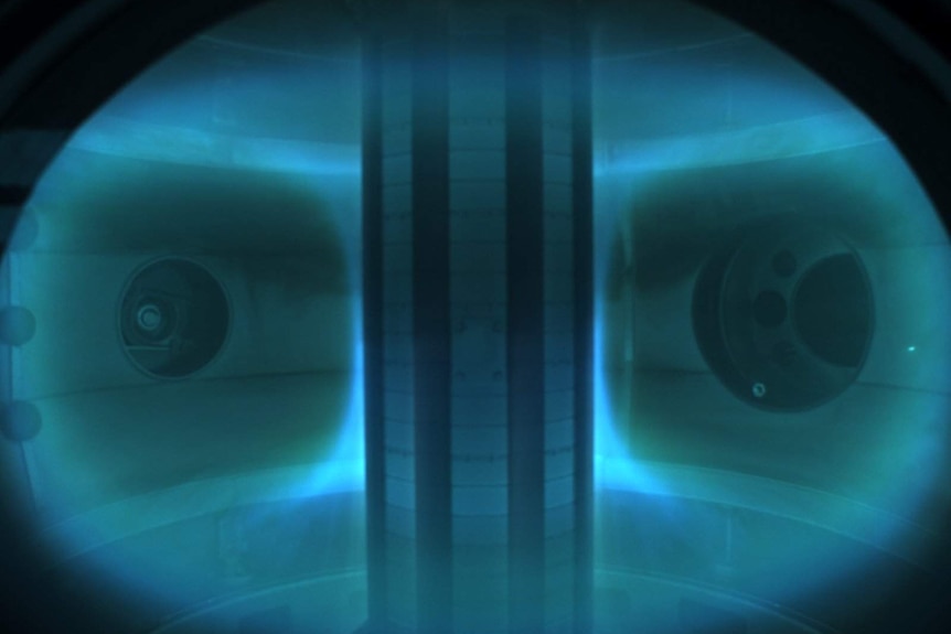 A blue glow can be seen inside the spherical tokamak device housing plasma.