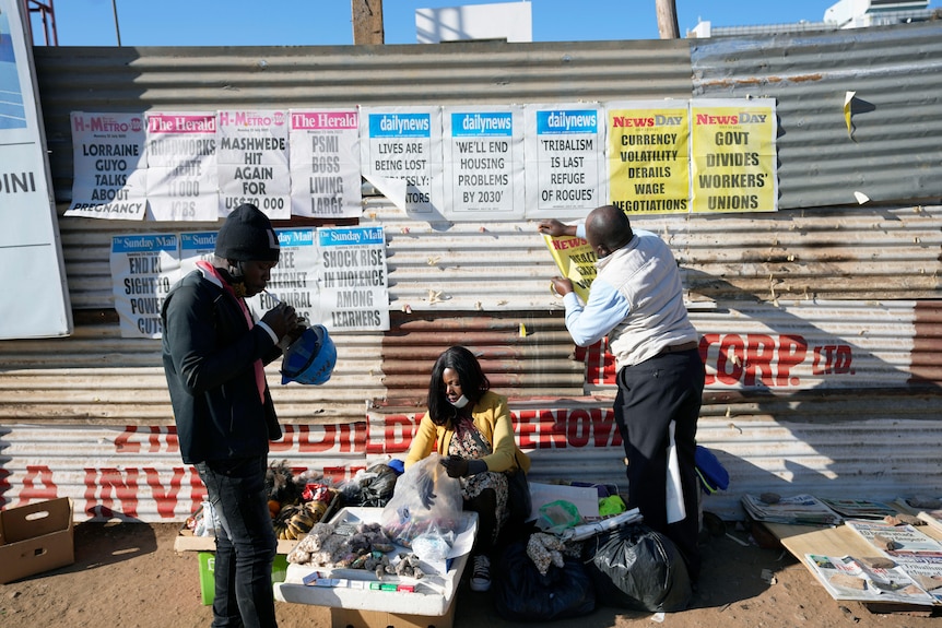 Un vendeur affiche des bannières de journaux alors qu'un vendeur se prépare à vendre, dans une rue