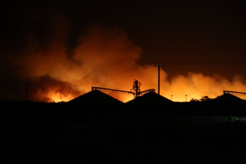 A red glow lights the horizon behind a grain processing plant.