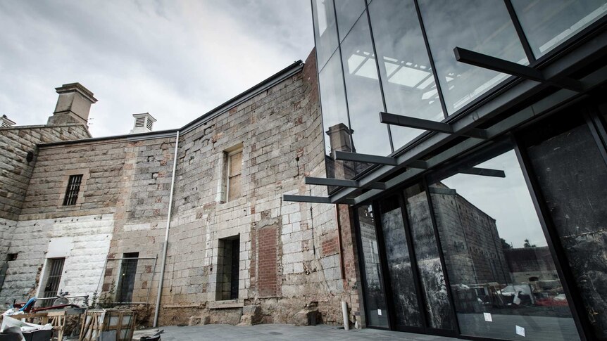 Image of an old stone wall, two stories high, meeting up with a sheer glass facade.