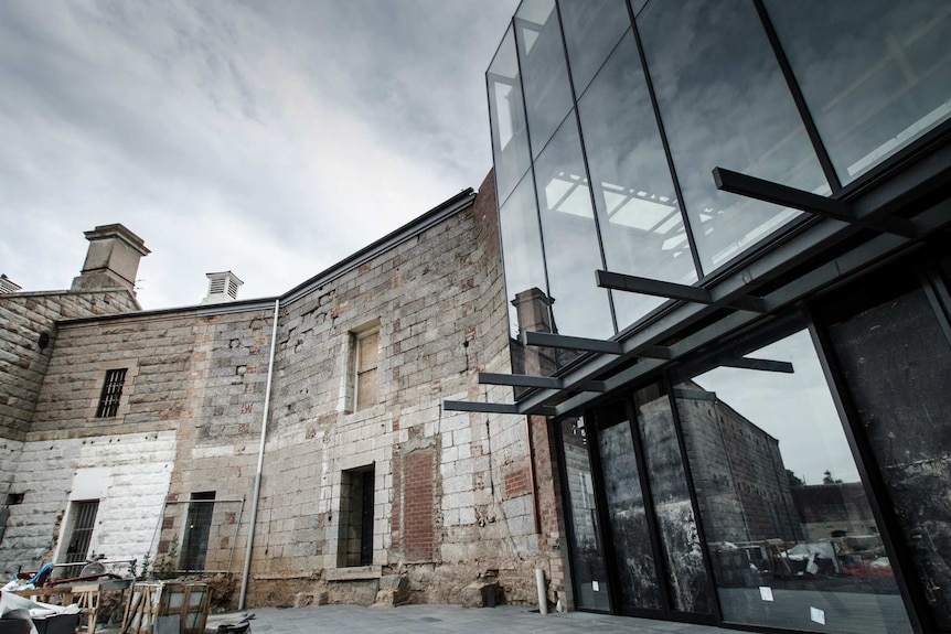 Image of an old stone wall, two stories high, meeting up with a sheer glass facade.