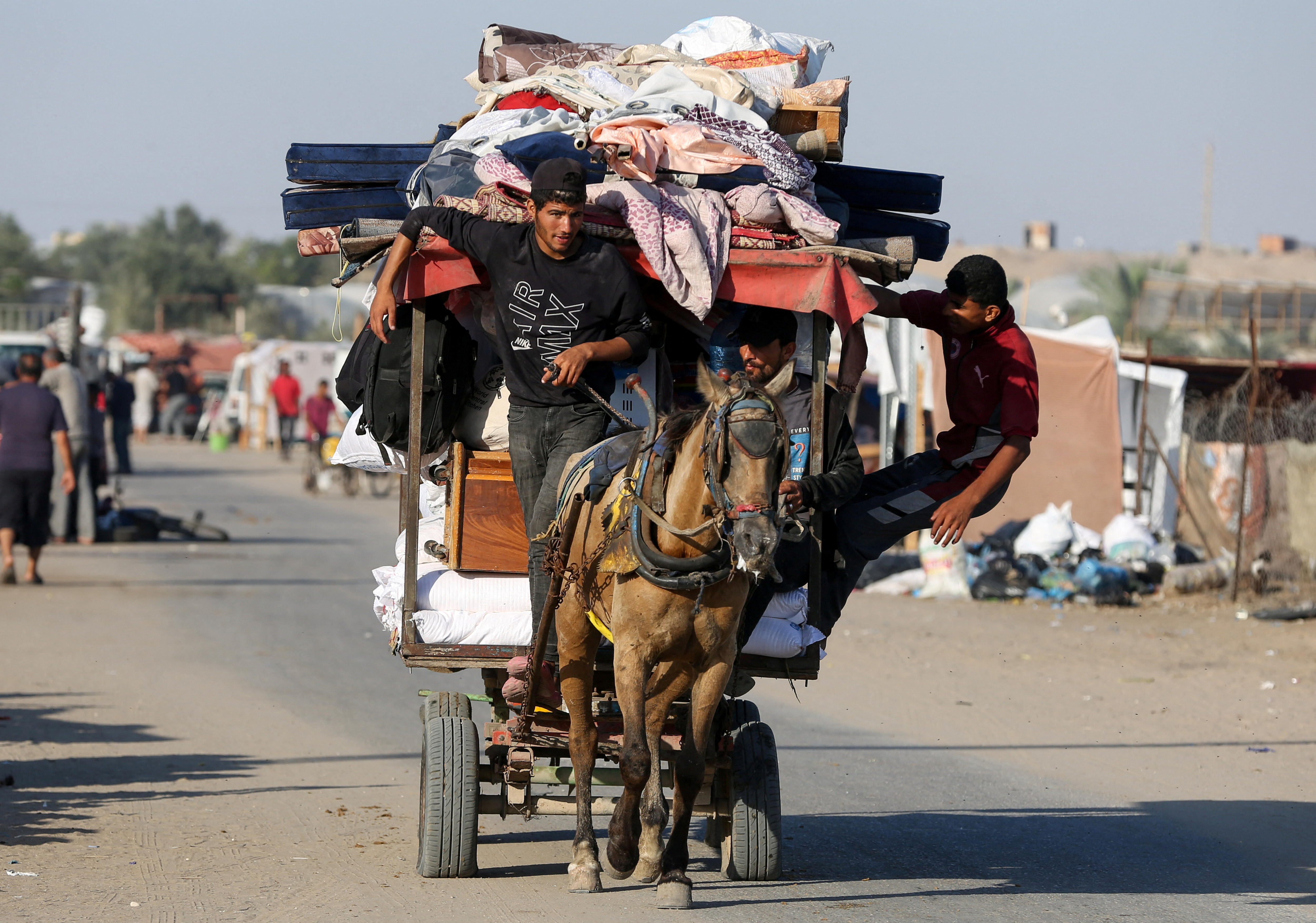 A man on a horse drawn cart with sheets and matresseson it. 