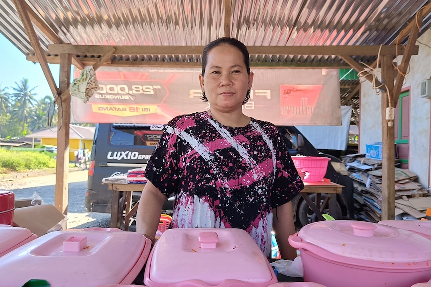 A woman stands in front of a table of food containers.