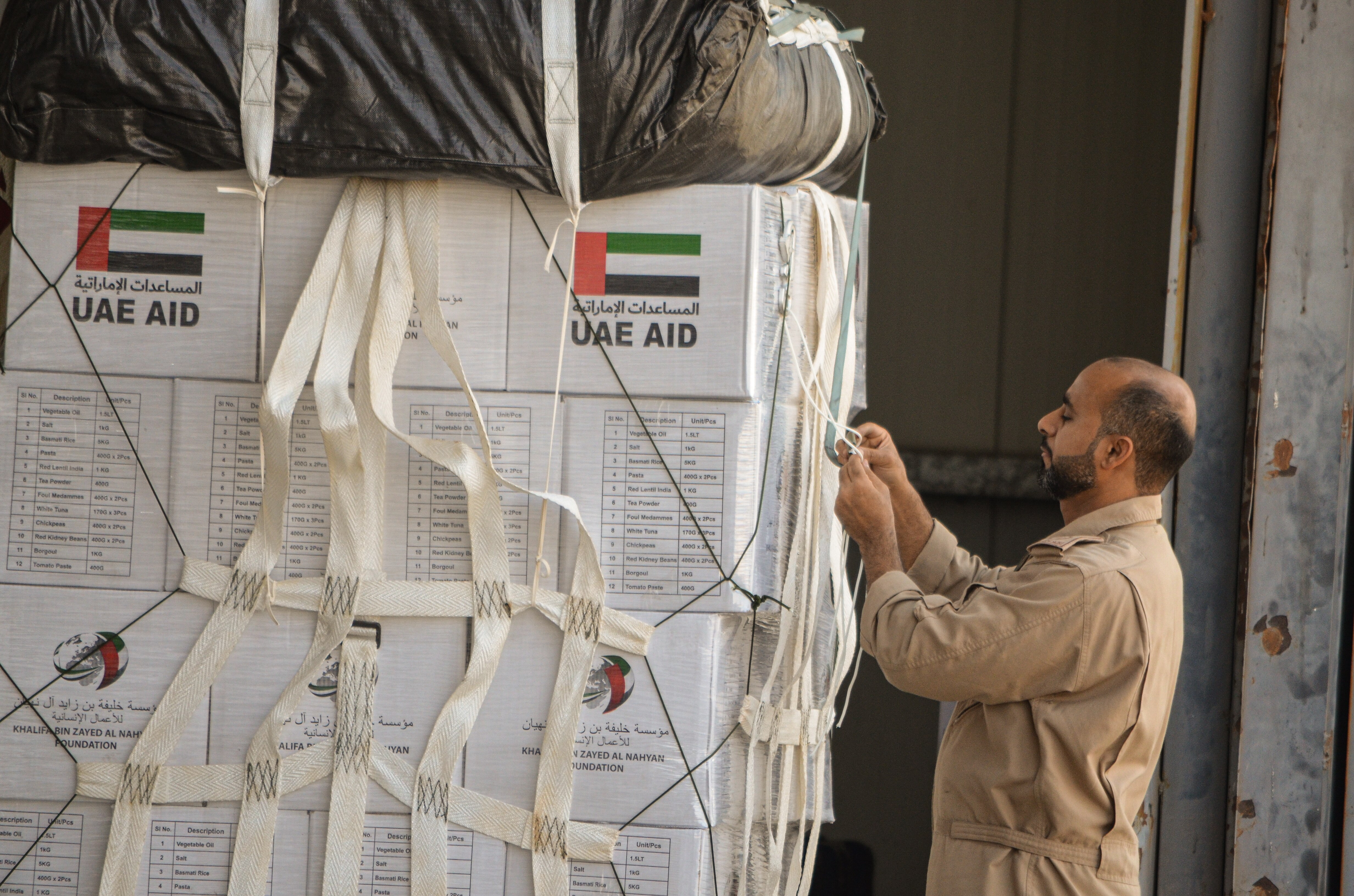 A man tethers a pallet of boxes of aid inside a military cargo plane.