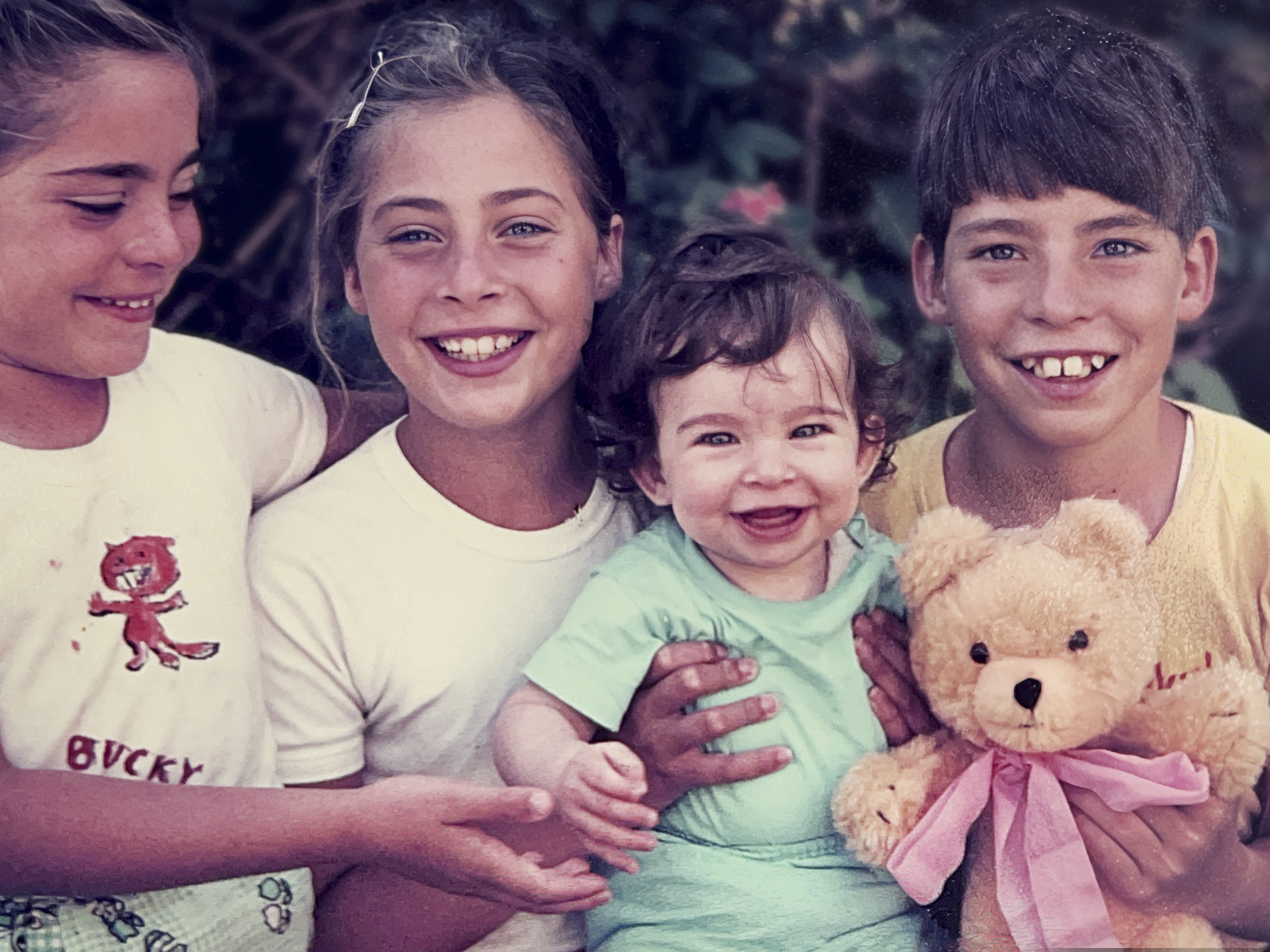 An old photo of four children, ranging in age from an infant to around 10 years old.