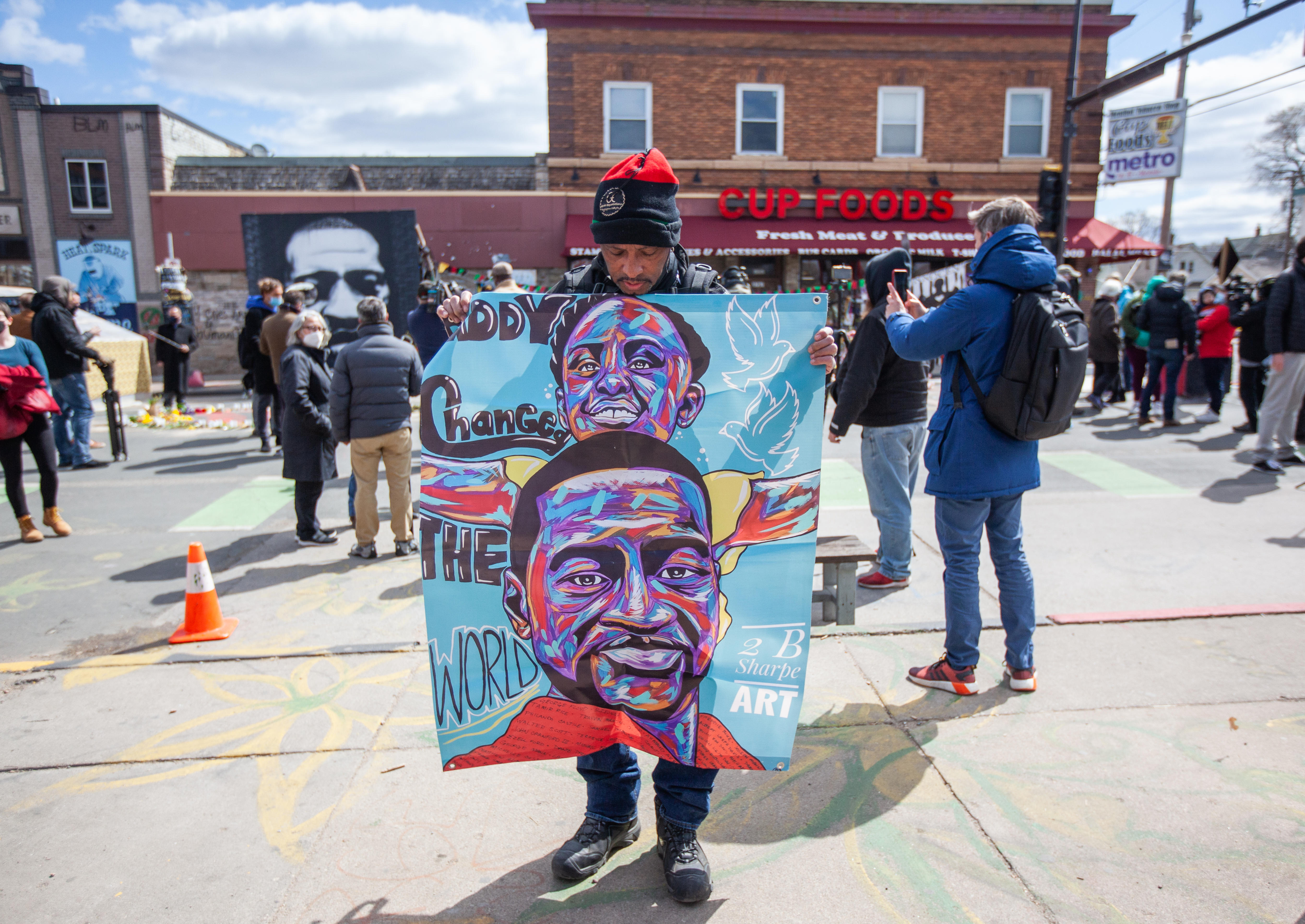A man holds a blue banner in the middle of a cluttered scene