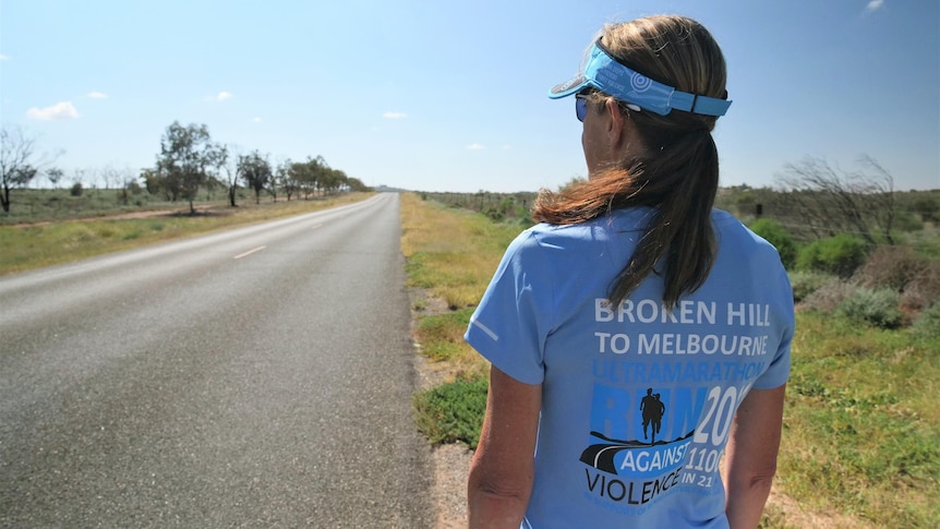 A woman in running attire staring at a long outback road.