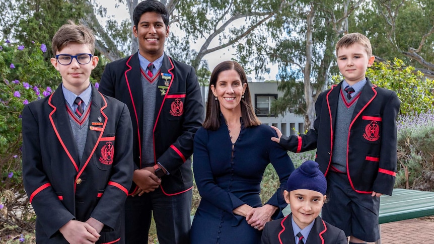 A woman with dark hair smiling and standing with four young male students.