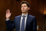 A white man in a suit holds up his hand and is sworn in 