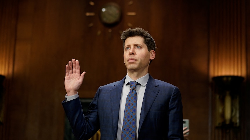 A white man in a suit holds up his hand and is sworn in 