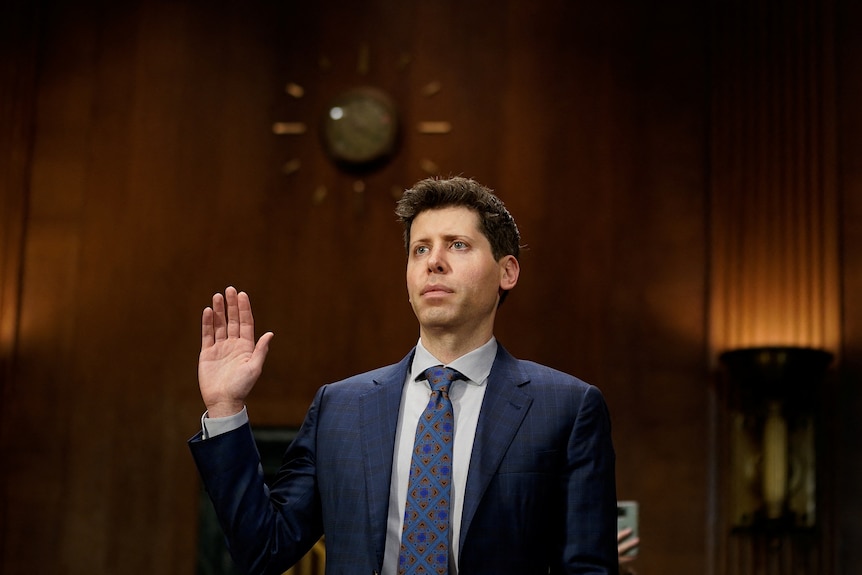 A white man in a suit holds up his hand and is sworn in 