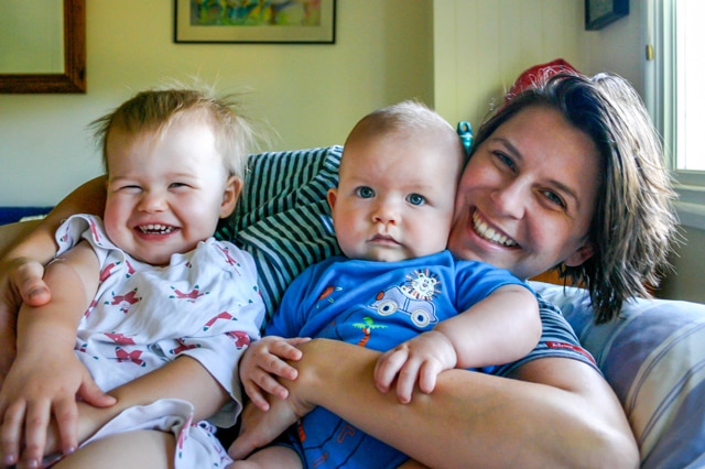 A woman lies on a bed holding two small children