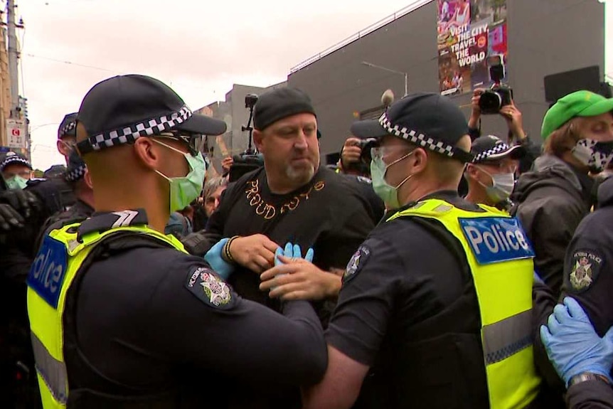 Police surround a man wearing a top bearing the words 'Proud Boys', in the intersection of Flinders and Swanston streets.