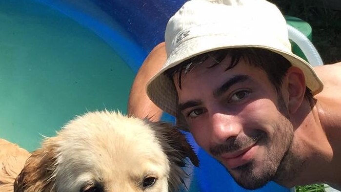 Colin Martin smiling beside a pool with a hat on posing next to a beautiful tan dog