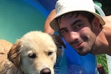Colin Martin smiling beside a pool with a hat on posing next to a beautiful tan dog