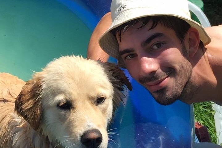 Colin Martin smiling beside a pool with a hat on posing next to a beautiful tan dog