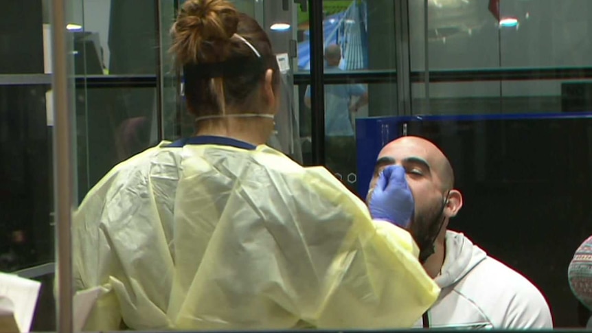 A woman hearing protective clothing puts a gloved hand up to the mouth of a man with a bald head