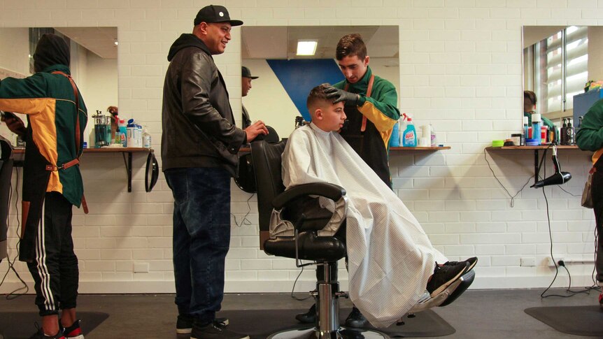 Project manager Charles Lomu standing behind a barbershop student, offering advice.