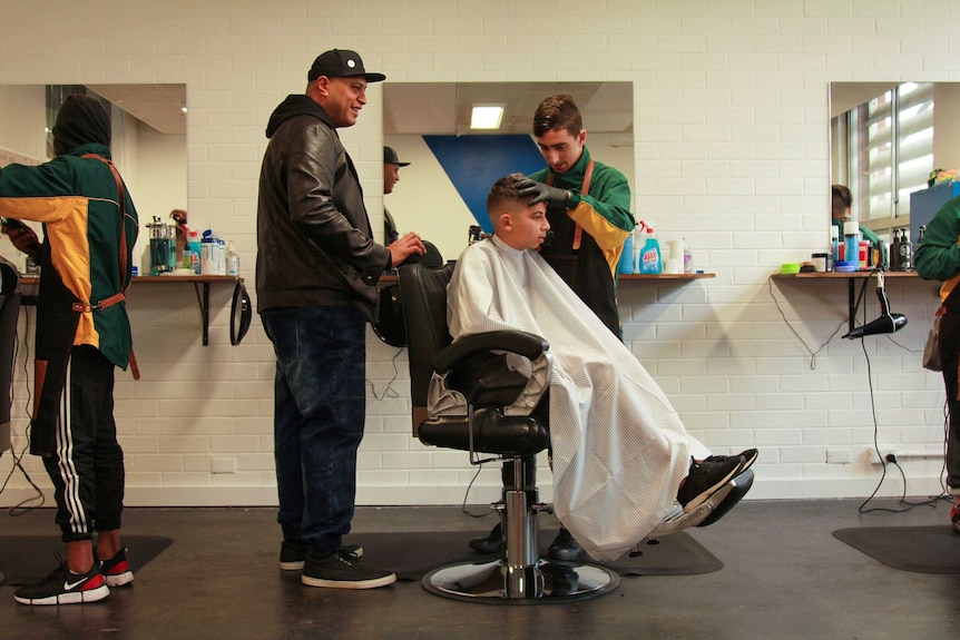 Project manager Charles Lomu standing behind a barbershop student, offering advice.