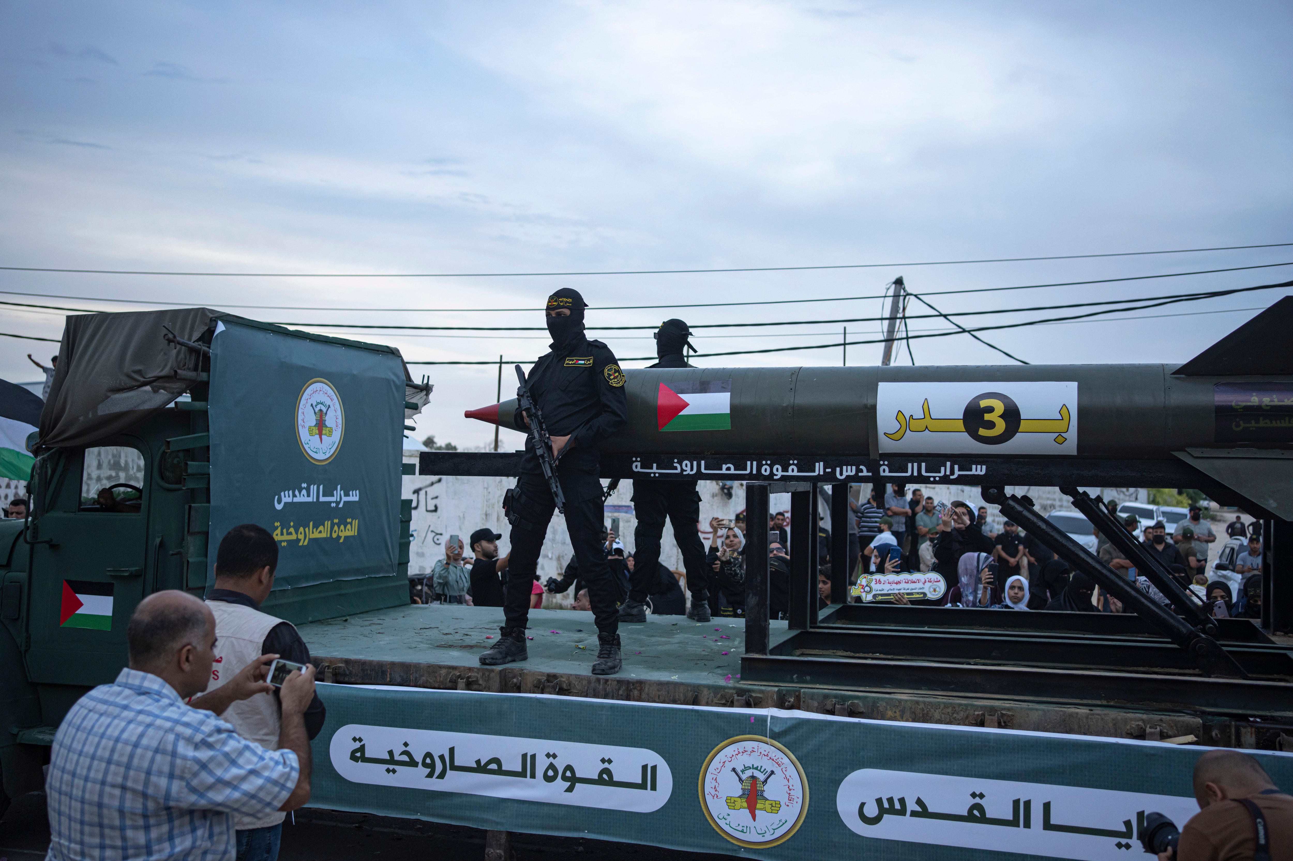 Two militants carrying guns and wearing face covering stand on the back of a truck in parade