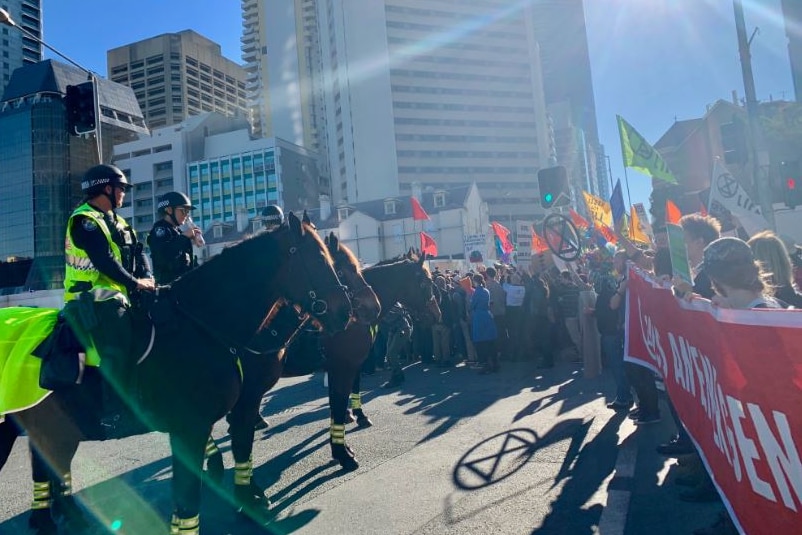 Mounted police face hundreds of protesters holding signs on a CBD street in Brisbane.
