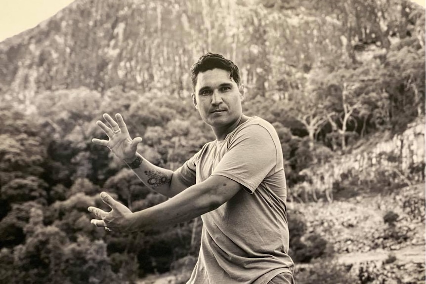 A black and white portrait of a Kiwi man standing in front of a mountain