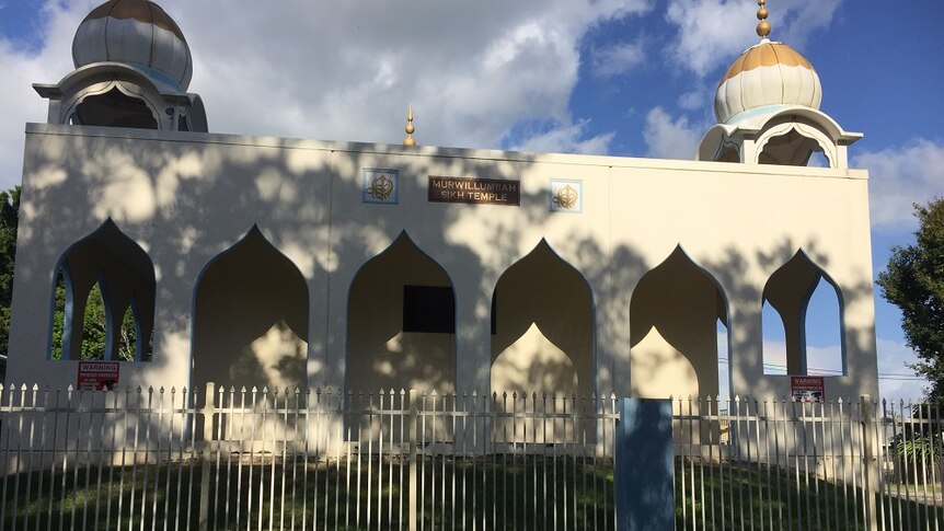A white building with dome shapes on either side with a sign saying, "Murwillumbah Sikh Temple".