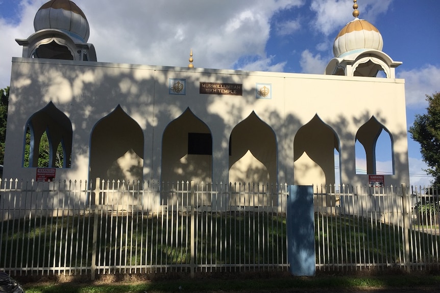 A white building with dome shapes on either side with a sign saying, "Murwillumbah Sikh Temple".