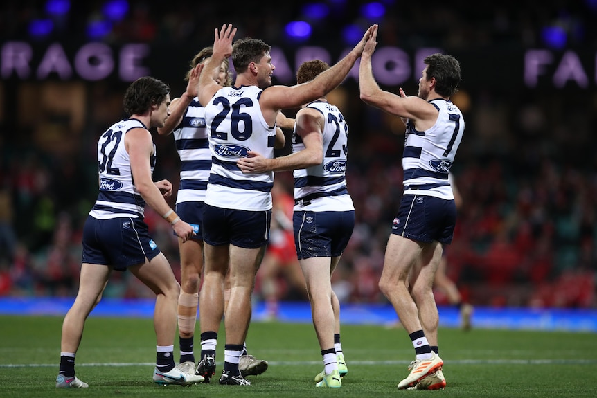 A group of Geelong players gather around a teammate to celebrate after a goal.